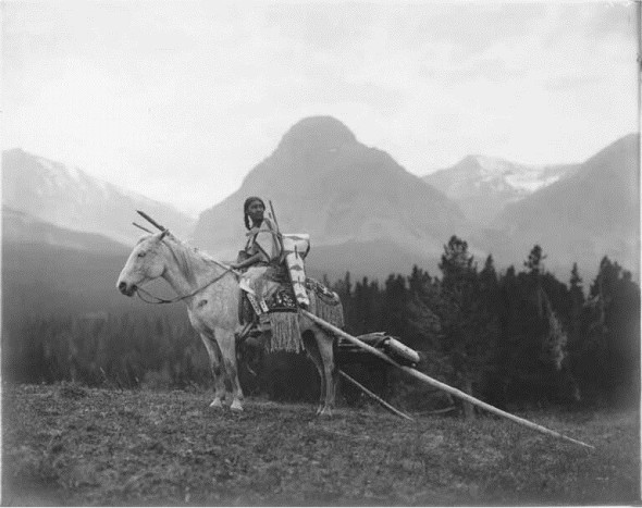 Piegan_Blackfeet_woman_on_a_horse_with_baby_carrier_cradle_board_and_travois_ca_19121915